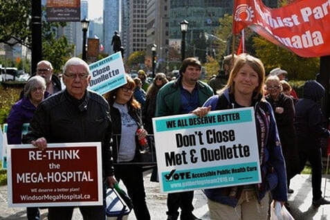 Two people in a rally holding signs that read re-think the megahospital and don't close Met and Ouellette